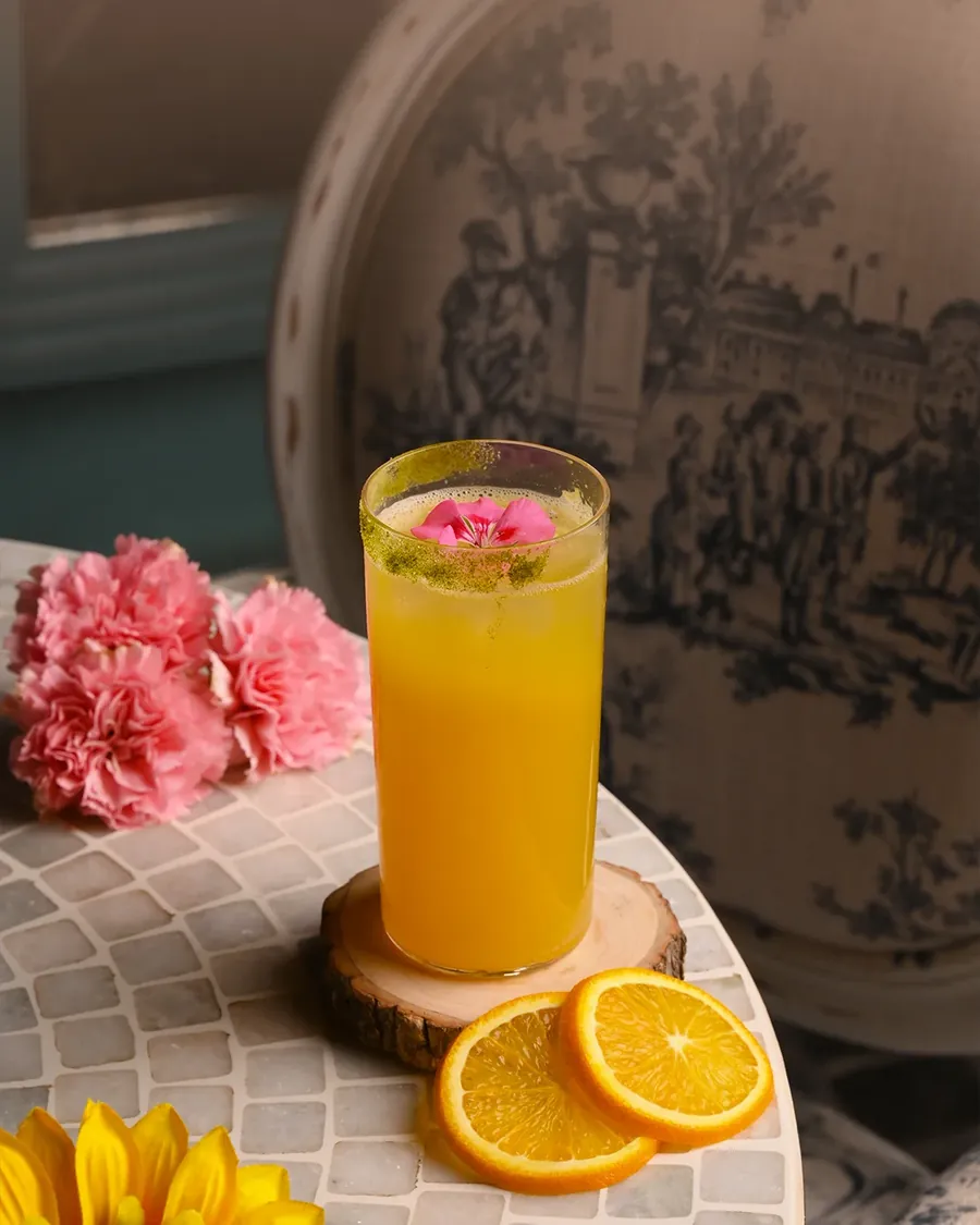 A fresh orange drink on a mosaic table with carnations